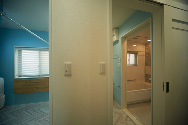写真：洗濯室と脱衣室はつながった空間の印象をもたせるため壁紙は同じ水色に。真ん中には両サイドから使える収納スペースを設けています。