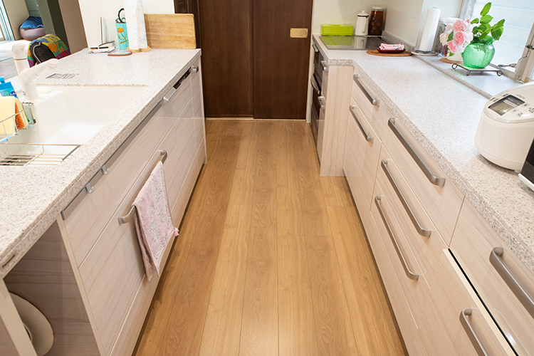 写真：木目のキッチン床と、白系に統一されたキッチンと収納カウンター
